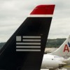 US Airways and American merger? A US Airways tail rest on the tarmac near two American Airlines planes.