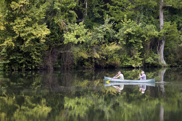 Two men canoing toward the bank of the lower segment of the Mountain Fork River near Beaver's Bend State Park.