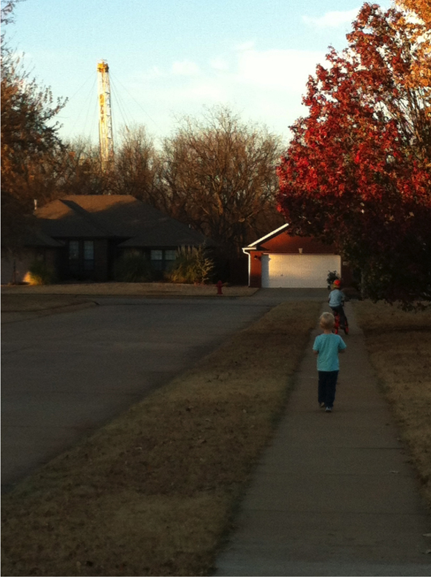 Tammy Mix's sons play on the sidewalk as a drilling rig peeks above the tree line behind her Stillwater home.