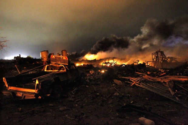 A vehicle is seen near the remains of a fertilizer plant burning after the explosion.