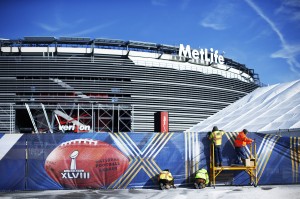 Workers prepare a fence with Super Bowl ads at the Metlife Stadium in East Rutherford, New Jersey, January 28, 2014. The stadium's solar panels are visible on the roof. 