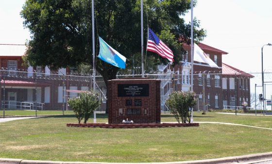 Flag Poles and a sign identifying Jess Dunn Correctional Center inside the prison's grounds.