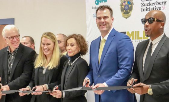 Gov. Kevin Stitt smiles while participating in a ribbon cutting ceremony.