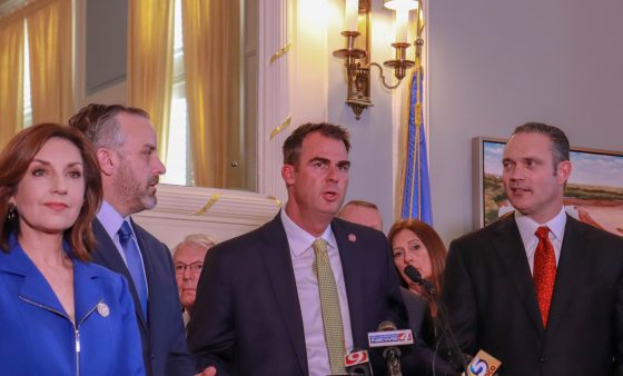 Gov. Kevin Stitt stands at a podium and announces a budget deal while flanked by legislative leaders.