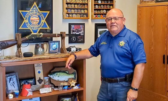 Sheriff Kelly Herzet stands next to a shelf in his office.