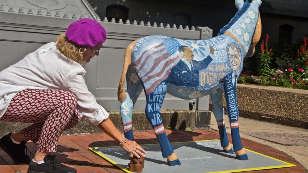 Tamara Clements with Food and Water Watch places dung beneath one of the DNC Donkeys Around Town sculptures. This donkey is at City Hall and represents Georgia.