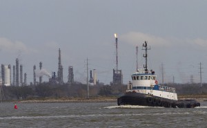  A tug boat navigates the Houston ship channel with a flare from an oil refinery and storage facility in the background south of downtown Houston